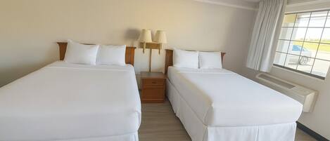 A hotel room with two beds, a nightstand with lamps, a window with curtains, and a radiator.