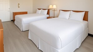 Une chambre d’hôtel avec deux lits, des têtes de lit en bois, du linge de lit blanc et des lampes de chevet.