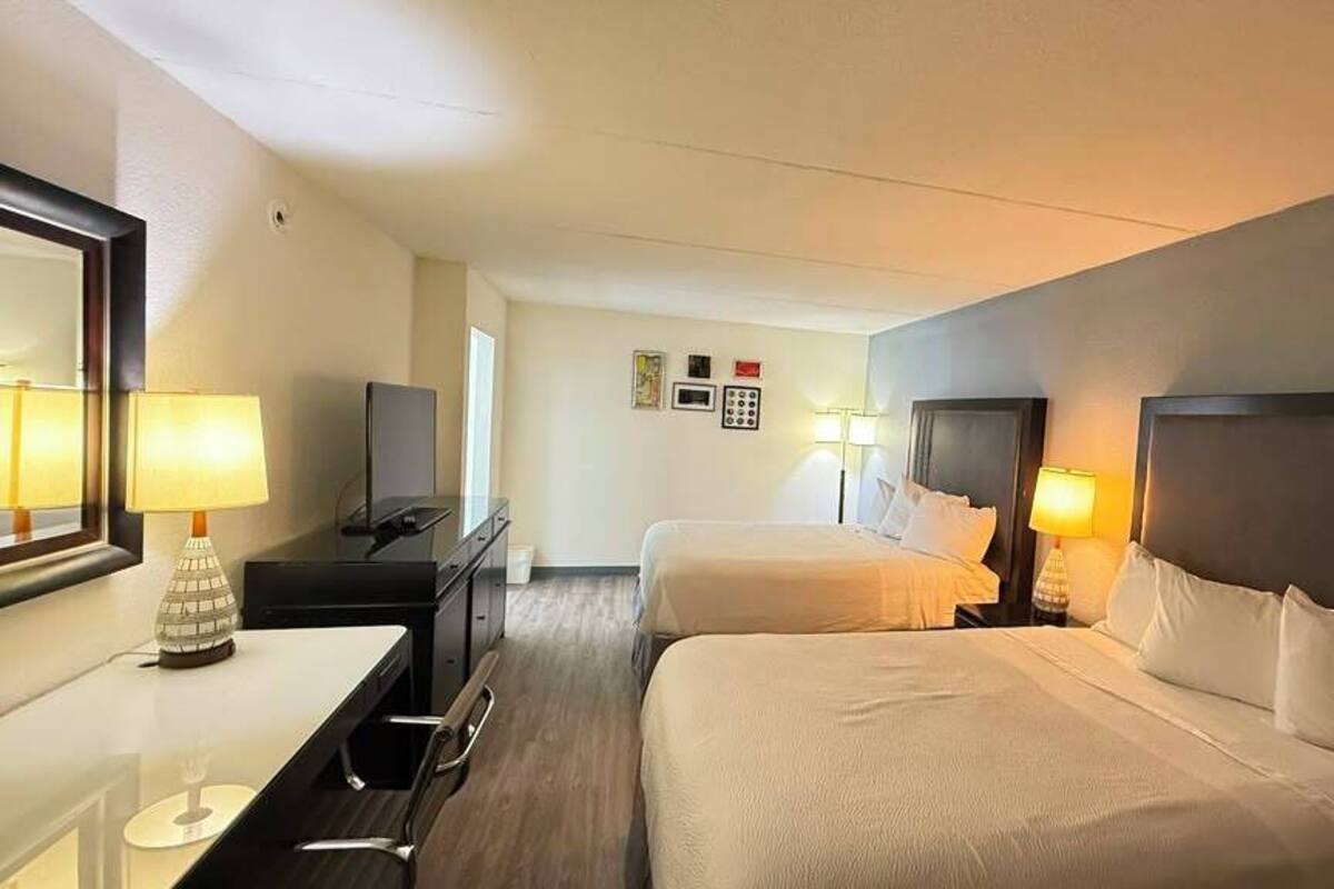 A hotel room with two beds, a desk, a chair, a TV, and a mirror.