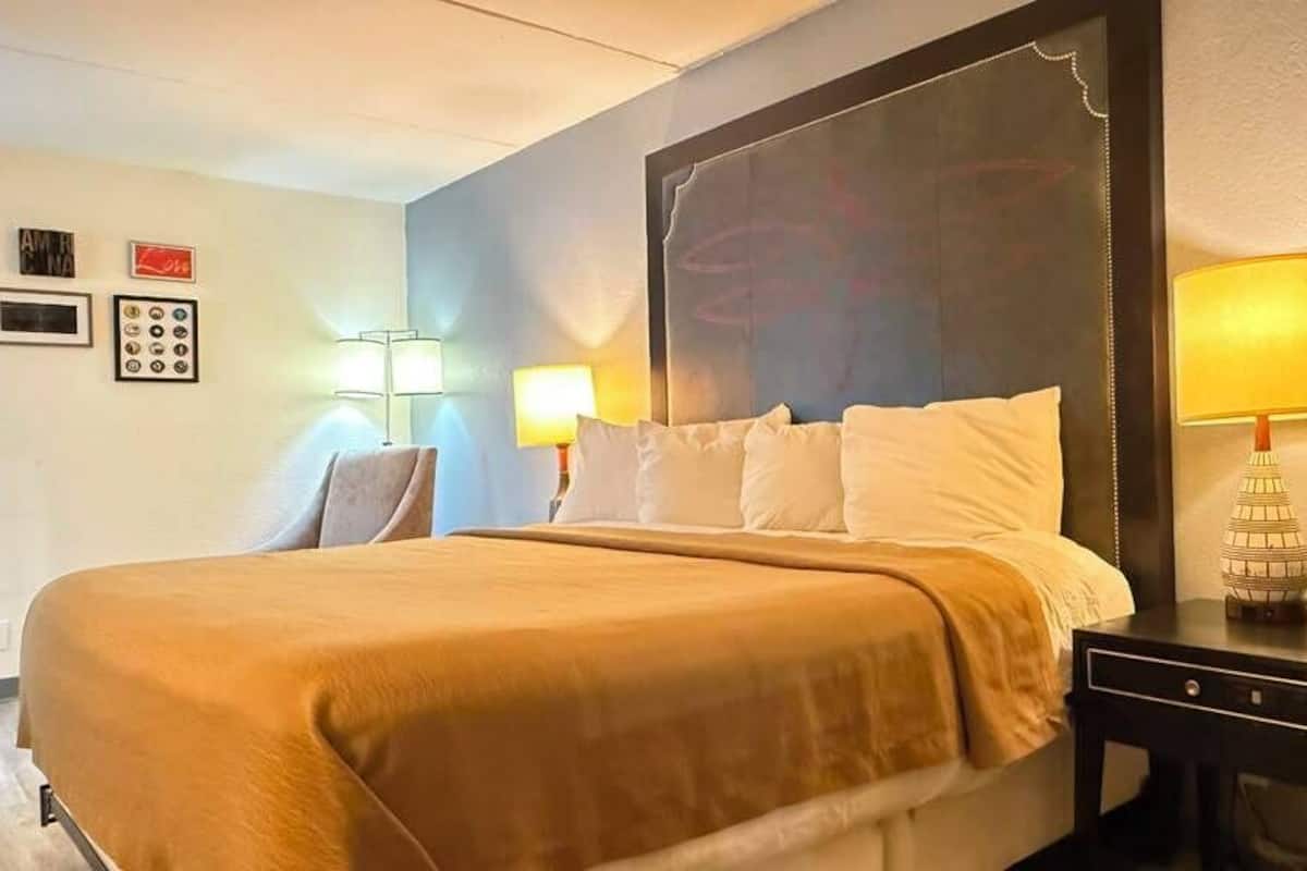 A hotel room with a large bed, two bedside lamps, a nightstand, and a wall-mounted clock.