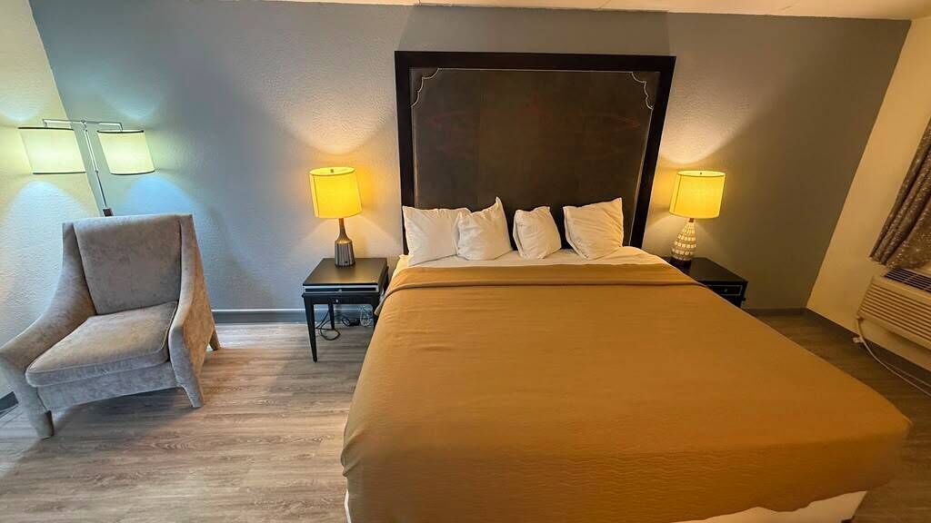 Ein Hotelzimmer mit einem Bett, zwei Nachttischen, einem Sessel und Lampen.