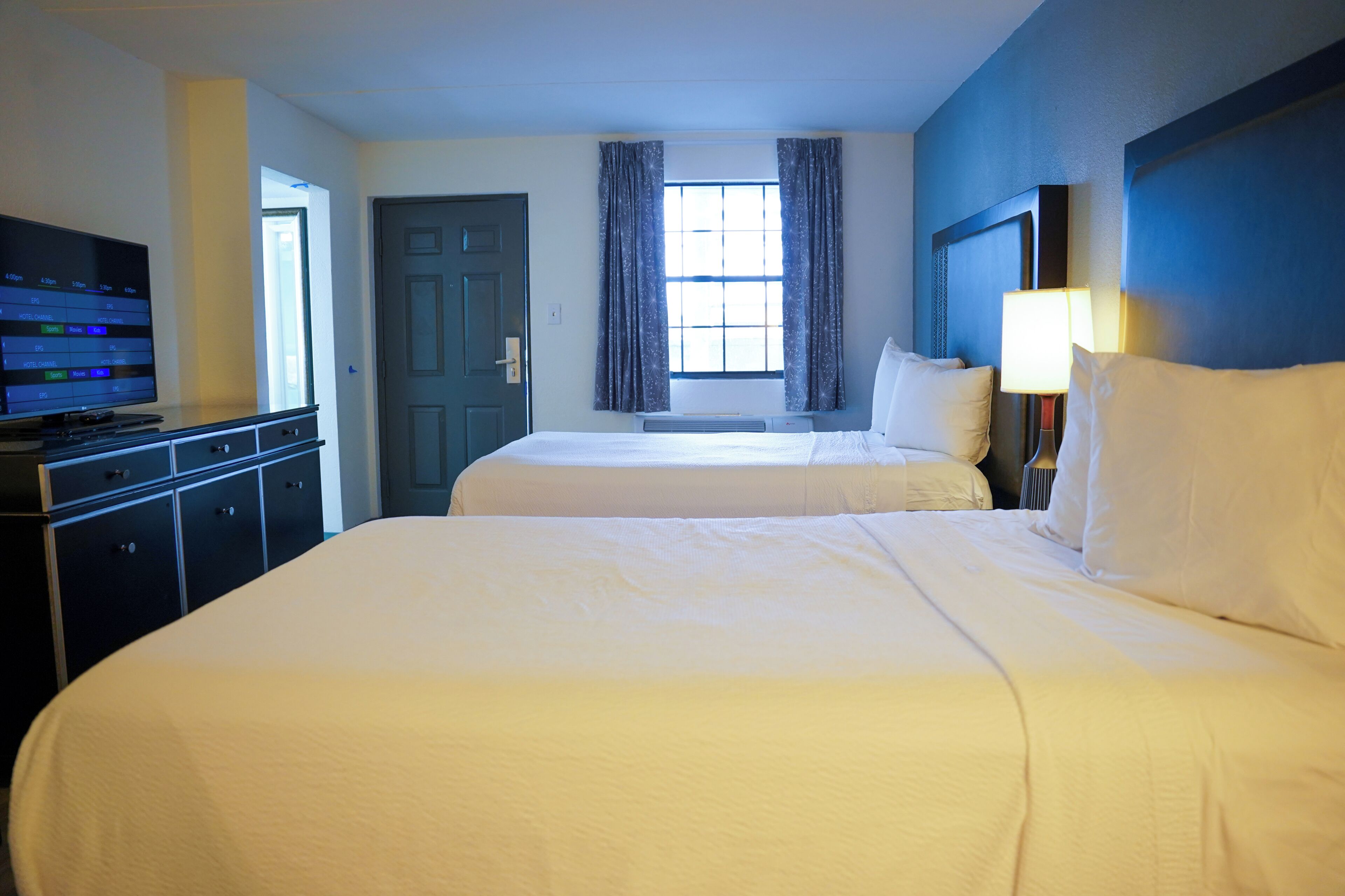 Habitación de hotel con dos camas, televisor, escritorio y ventana con cortinas.