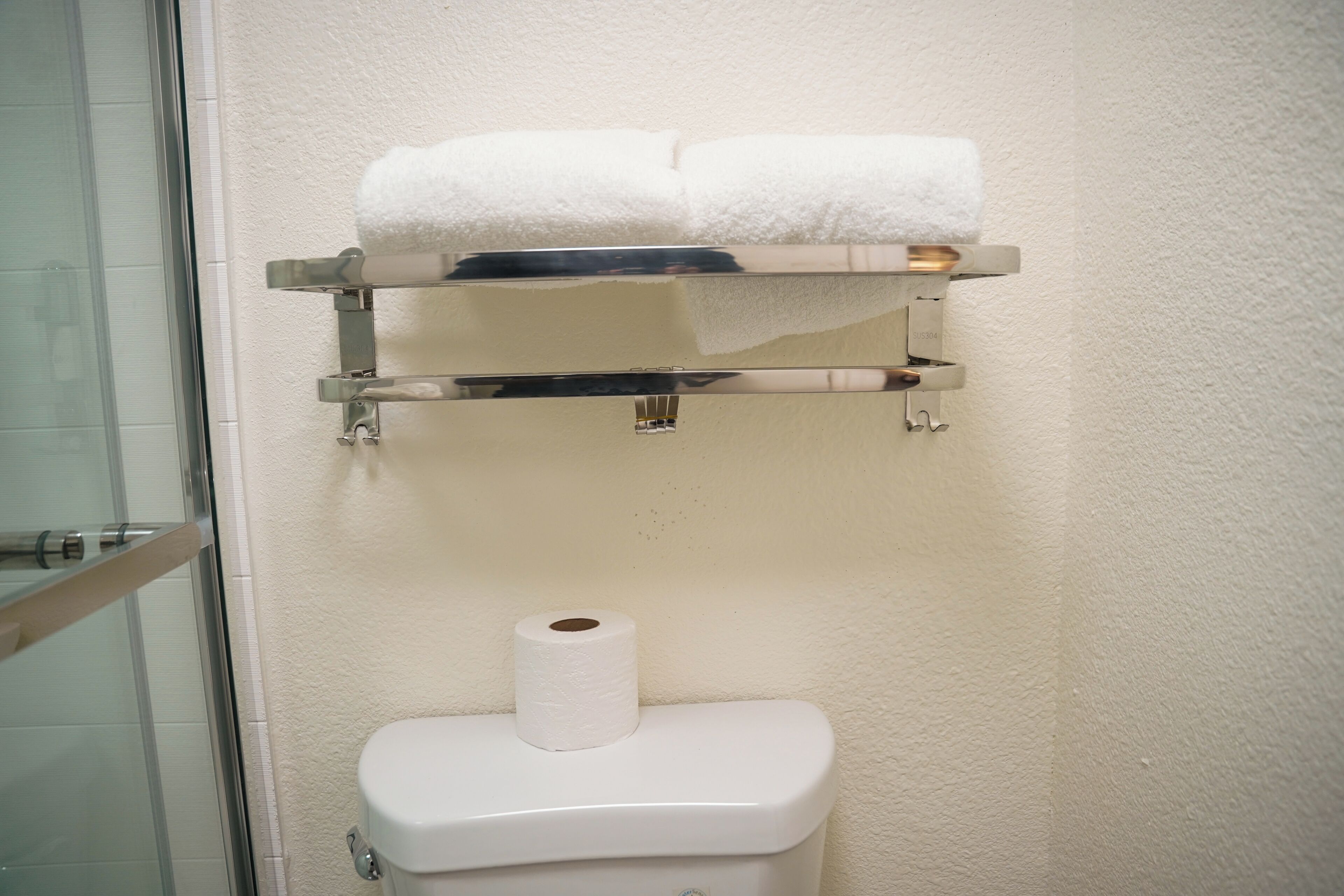 A bathroom with a toilet, a paper towel holder, and a glass shower enclosure.