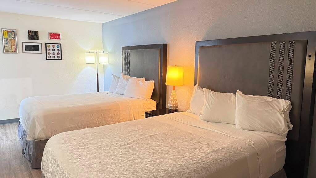 Habitación de hotel con dos camas, cada una con cabecero, lámparas de noche y un reloj de pared.