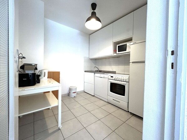 A compact kitchen with white cabinets, a built-in microwave, a stove, and a refrigerator.