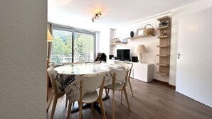 A dining area with a round table and chairs, a television, and a shelf with decorative items.