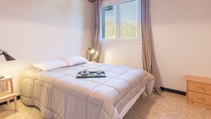 A bedroom with a bed, bedside table, lamp, and a window with curtains.