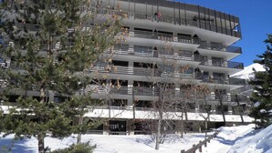 A multi-story building with balconies and a snow-covered ground.