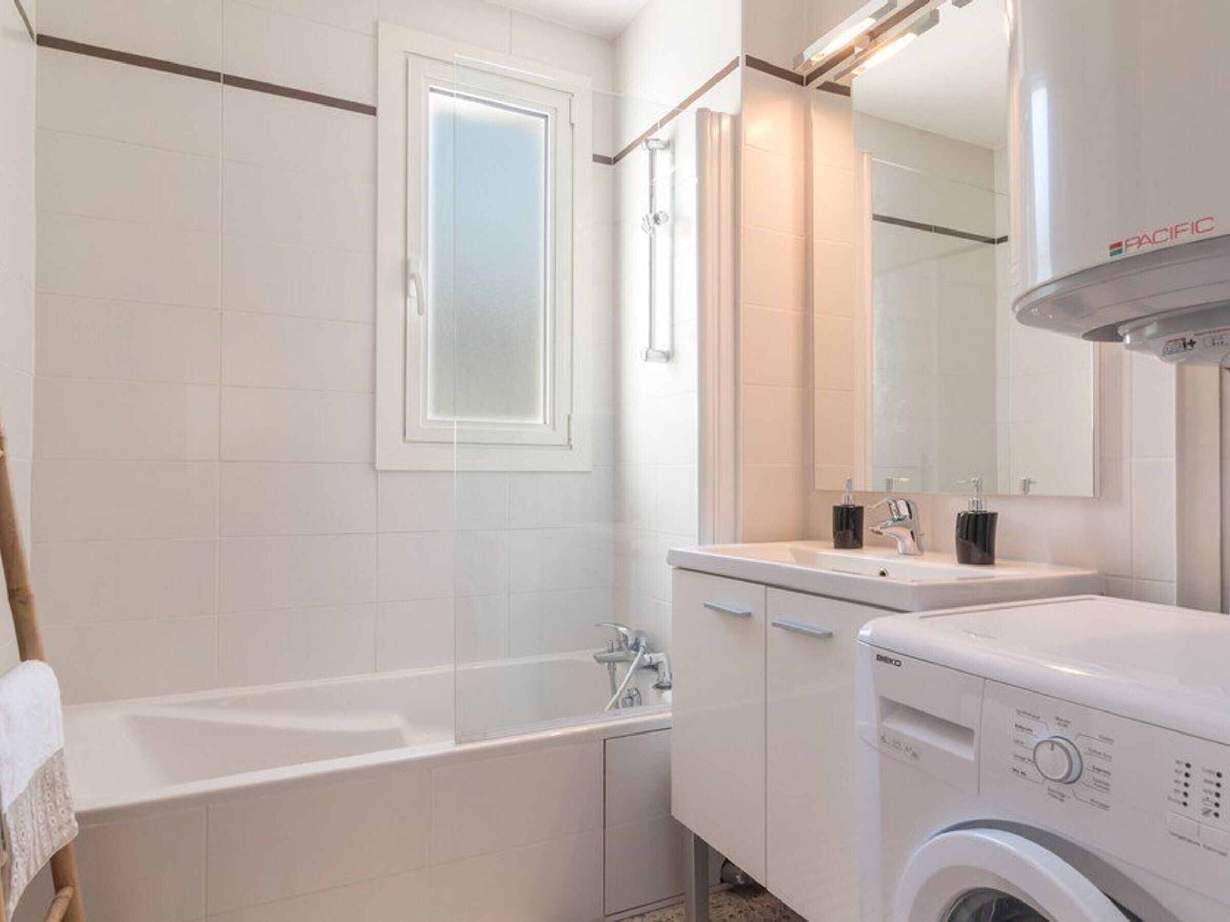A modern bathroom with a bathtub, a washing machine, and a sink with a mirror above it.