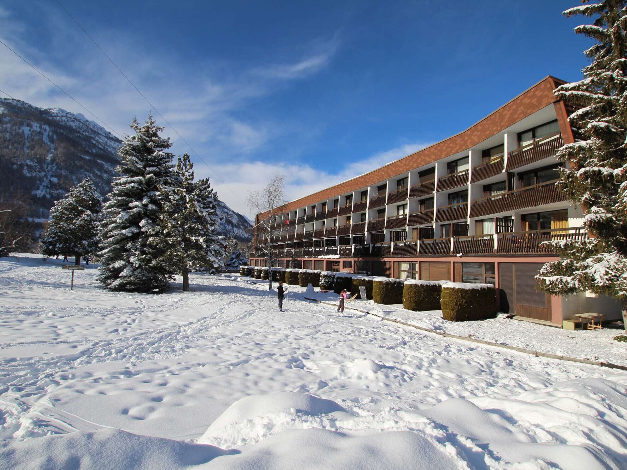 Ett hotell med flera våningar och balkonger, omgivet av snötäckta träd och berg.