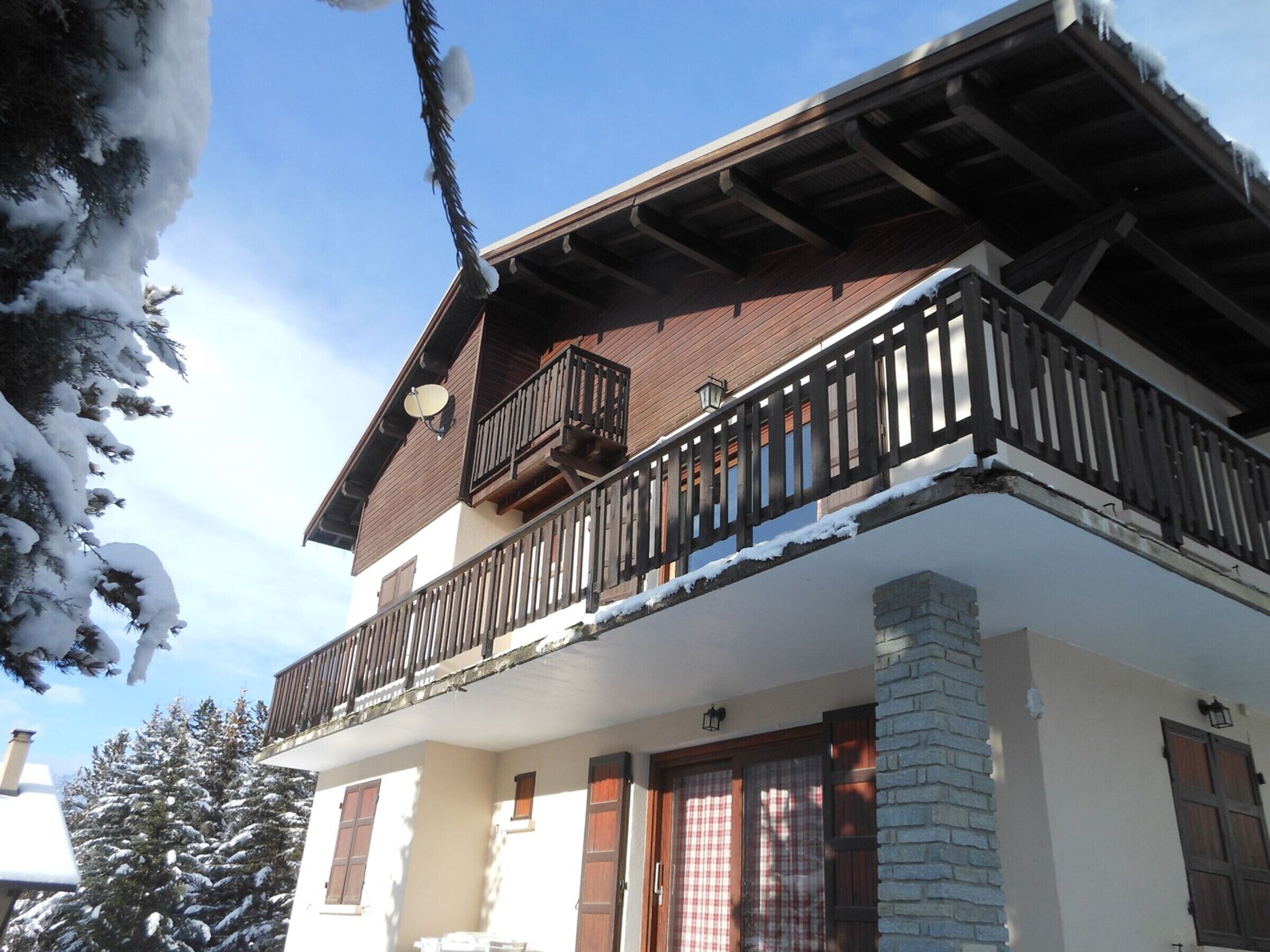 Un edificio a due piani con un balcone, travi in legno e alberi ricoperti di neve.