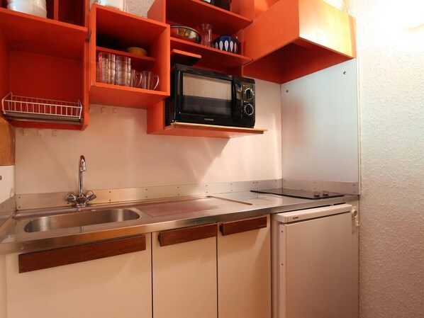 A compact kitchen with a stainless steel sink, a microwave, and orange storage shelves.