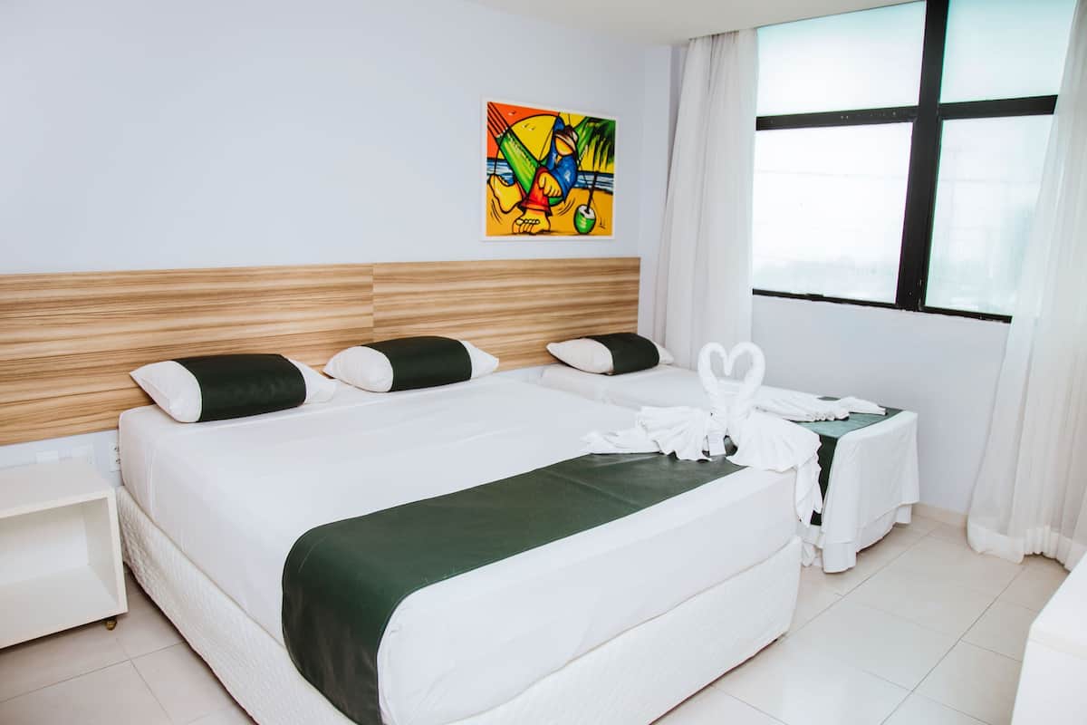 A hotel room with a large bed, a nightstand, a small table with a telephone, and a window with curtains.