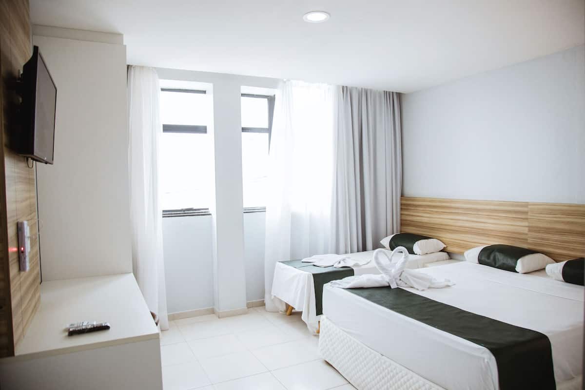 A hotel room with a bed, a small table, a TV, and a window with curtains.