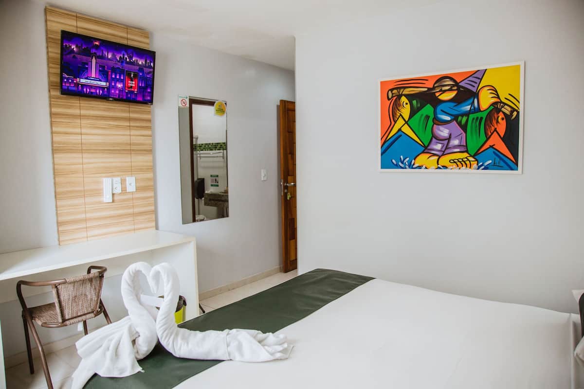 A hotel room with a bed, a TV mounted on the wall, a painting, and a chair.