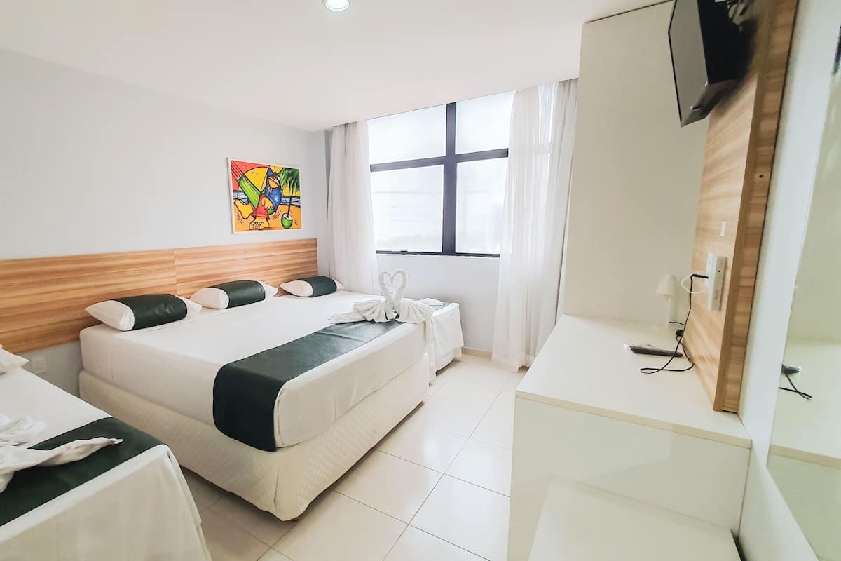 A hotel room with two beds, a wooden headboard, a large window with curtains, a painting on the wall, and a desk with a mirror and a phone.
