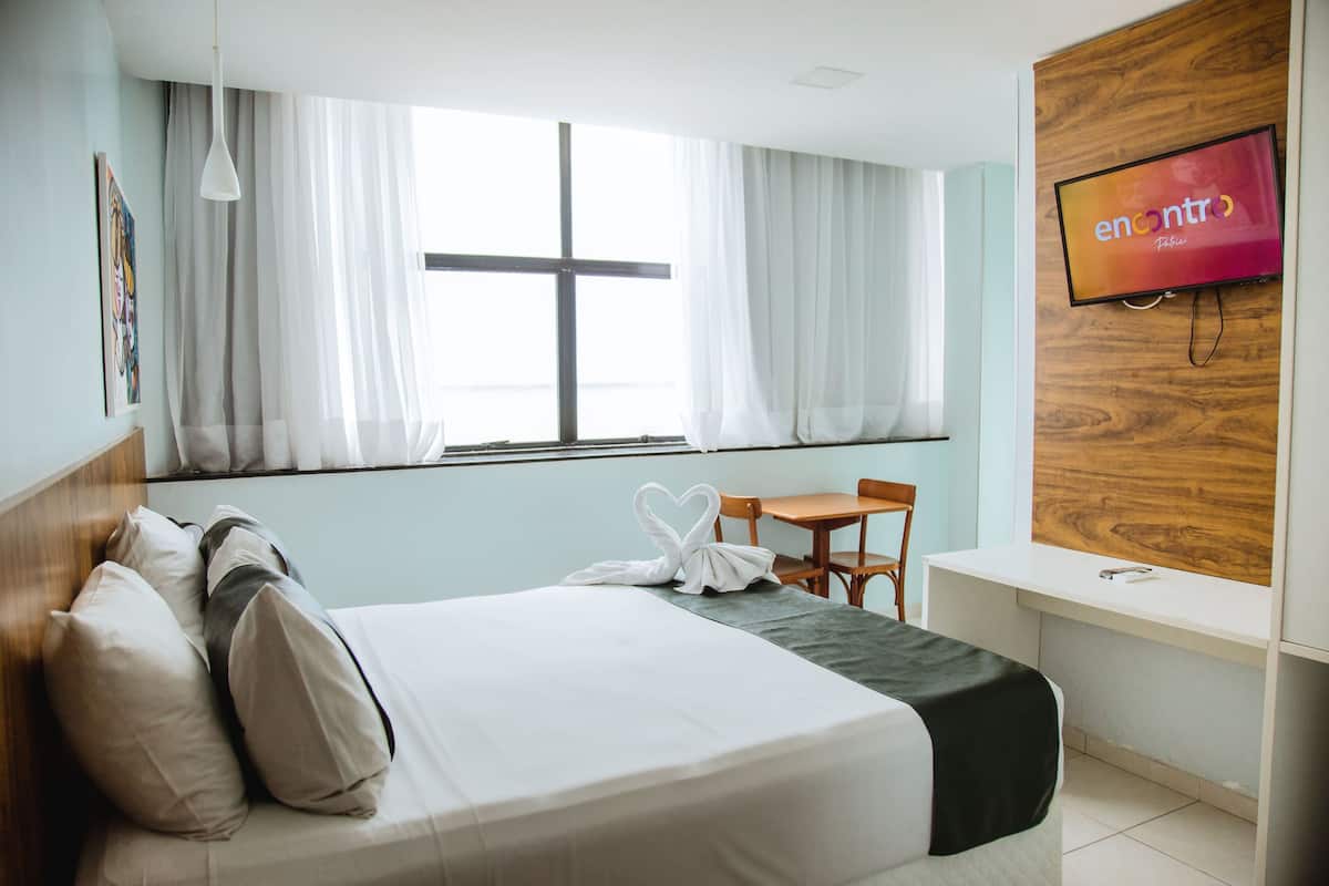A hotel room with a bed, a desk, a chair, a TV, and a window with curtains.