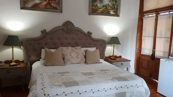 A neatly arranged bedroom with a large bed, two bedside tables with lamps, a wooden door, and two landscape paintings on the wall.