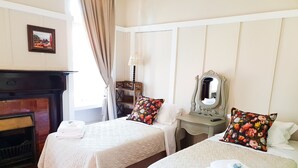Quarto de hotel com duas camas, lareira, espelho e janela com cortinas.