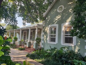 Una casa verde con porche cubierto, columnas blancas y un camino de piedra que lleva a la entrada.