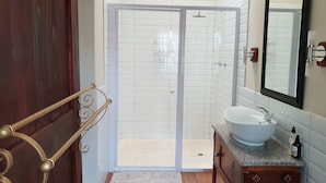 Uma casa de banho com lavatório branco, espelho e zona de duche com azulejos brancos.