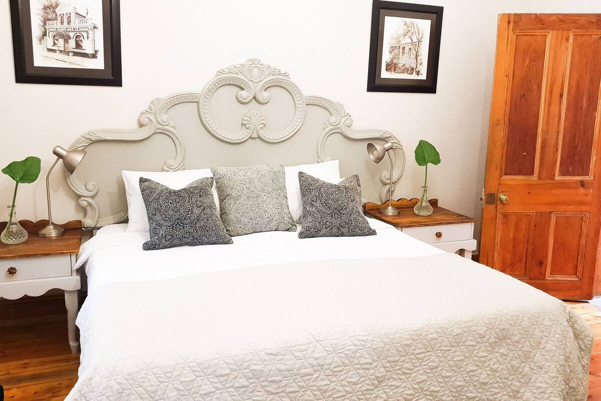 Una cama bien hecha con almohadas estampadas, una lámpara de noche y un cuadro en el mesita de noche.