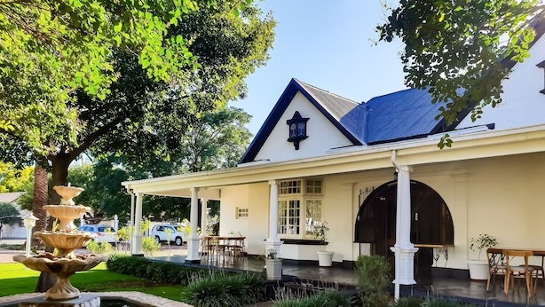 Um edifício com alpendre coberto, fonte de pedra e um gramado bem cuidado.