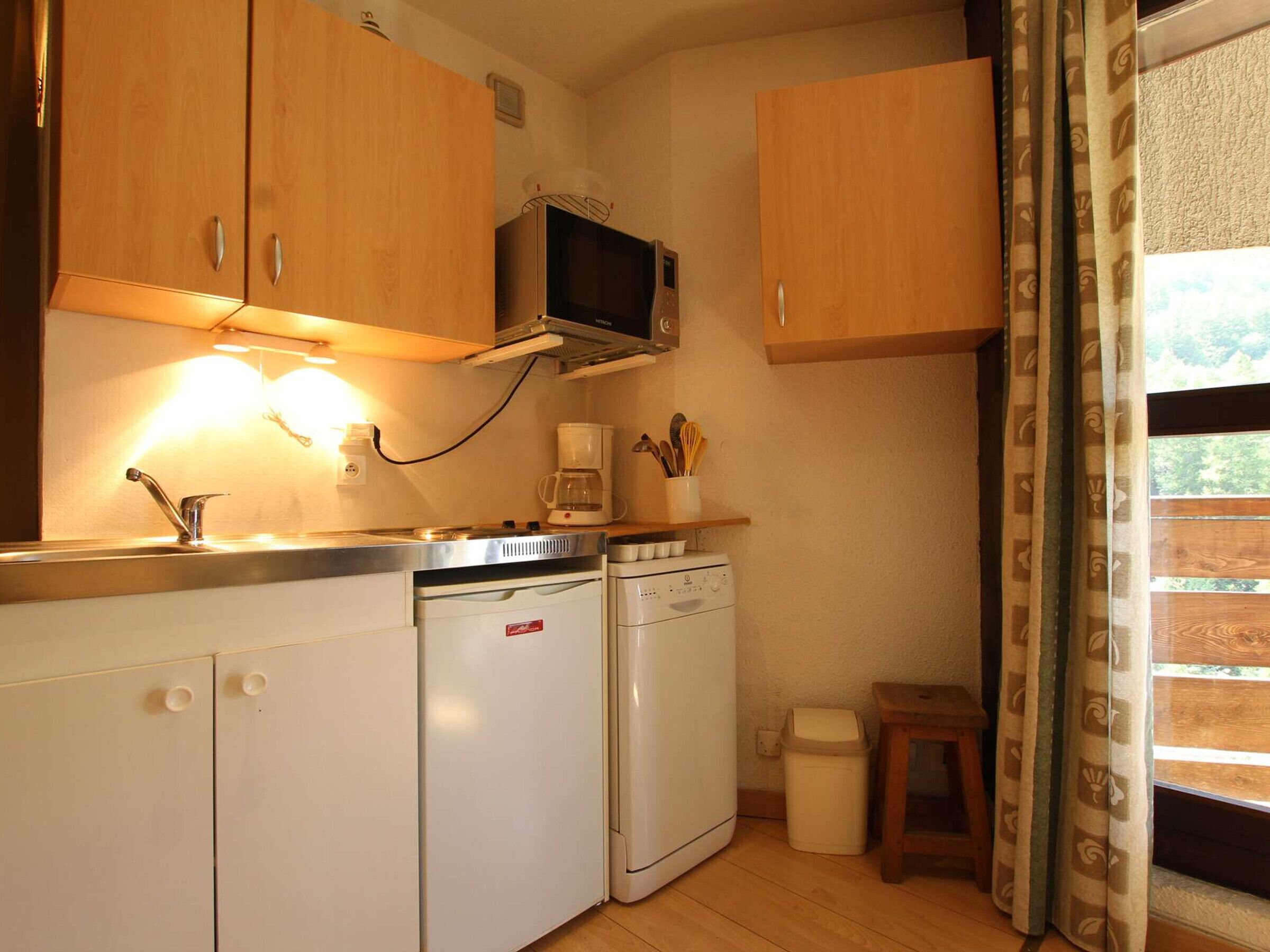 A compact kitchen with wooden cabinets, a microwave, a coffee maker, and a dishwasher.