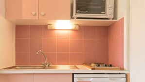 A compact kitchen with pink tiles, a built-in microwave, a sink, and a dishwasher.