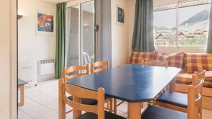 A dining area with a table and chairs, a sofa, and a view of a mountainous landscape through large windows.