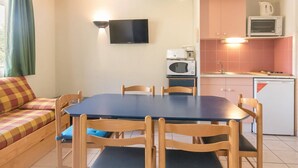 A compact living space with a sofa, dining table, chairs, a television, a microwave, and a small kitchen area.
