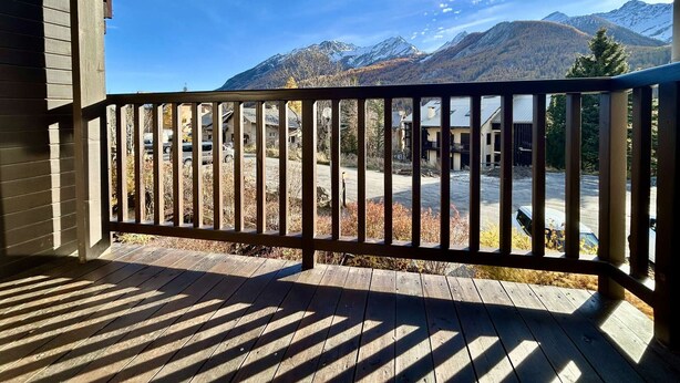 A wooden deck with a view of a mountain range and a parking area.