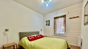 A bedroom with a bed, a nightstand, a window with curtains, and a picture on the wall.