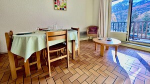 A dining area with a table set for two, a wicker chair, and a small round table with a cup and saucer.