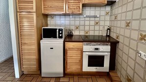 A compact kitchen with wooden cabinets, a microwave, a refrigerator, and an oven.