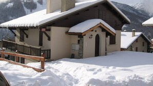 Un chalet enneigé, doté d’une façade en pierre, de poutres en bois et d’un toit à forte pente.