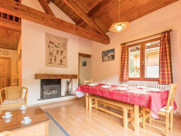 A dining area with a wooden table set for four, a fireplace, and a window with curtains. - Spacious Chalet for 8 with Fireplace and Mountain Views, Saint-Chaffrey, Serre-Chevalier (Saint-Chaffrey)