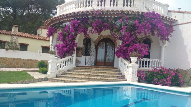 A poolside view of a building with a white facade, a stone staircase leading to the entrance, and vibrant purple flowers. - Detached villa for 6 people located in Miami Playa (MIAMI PLAYA)
