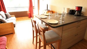A dining area with a table set for two, a coffee maker, and a bottle on the counter. - Cozy Mountain Studio for 4 with Ski-In Access and Seasonal Pool (La Salle-les-Alpes)