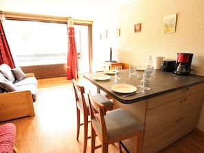 Un comedor con una mesa para dos, una cafetera y una botella en la encimera.