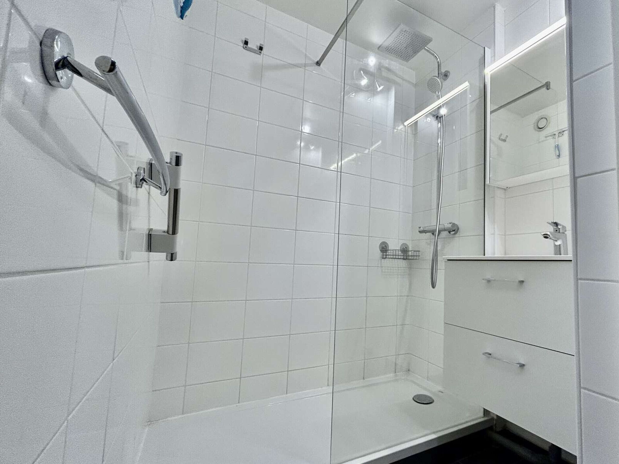 A modern bathroom with a glass shower enclosure, chrome fixtures, and a white tiled floor.