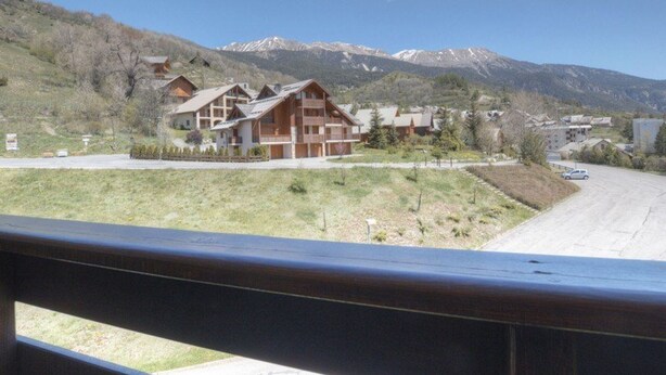 A mountain lodge with multiple wooden buildings, a grassy area in front, and a road with a car.