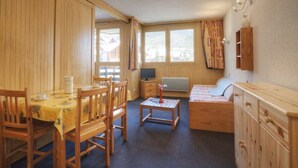 A cozy room with a wooden dining table, chairs, a small TV, a sofa, and a cabinet.