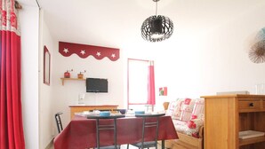 A dining area with a table set for two, a television on the wall, and a sofa with a patterned cover.