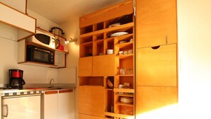 Een kleine keuken met houten kastjes, een magnetron, een koffiezetapparaat en een koelkast.