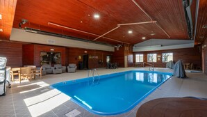 Une piscine intérieure aux murs et au plafond en bois, un espace de détente avec des fauteuils et des tables, et un espace extérieur aménagé avec des sièges, protégé par un toit.