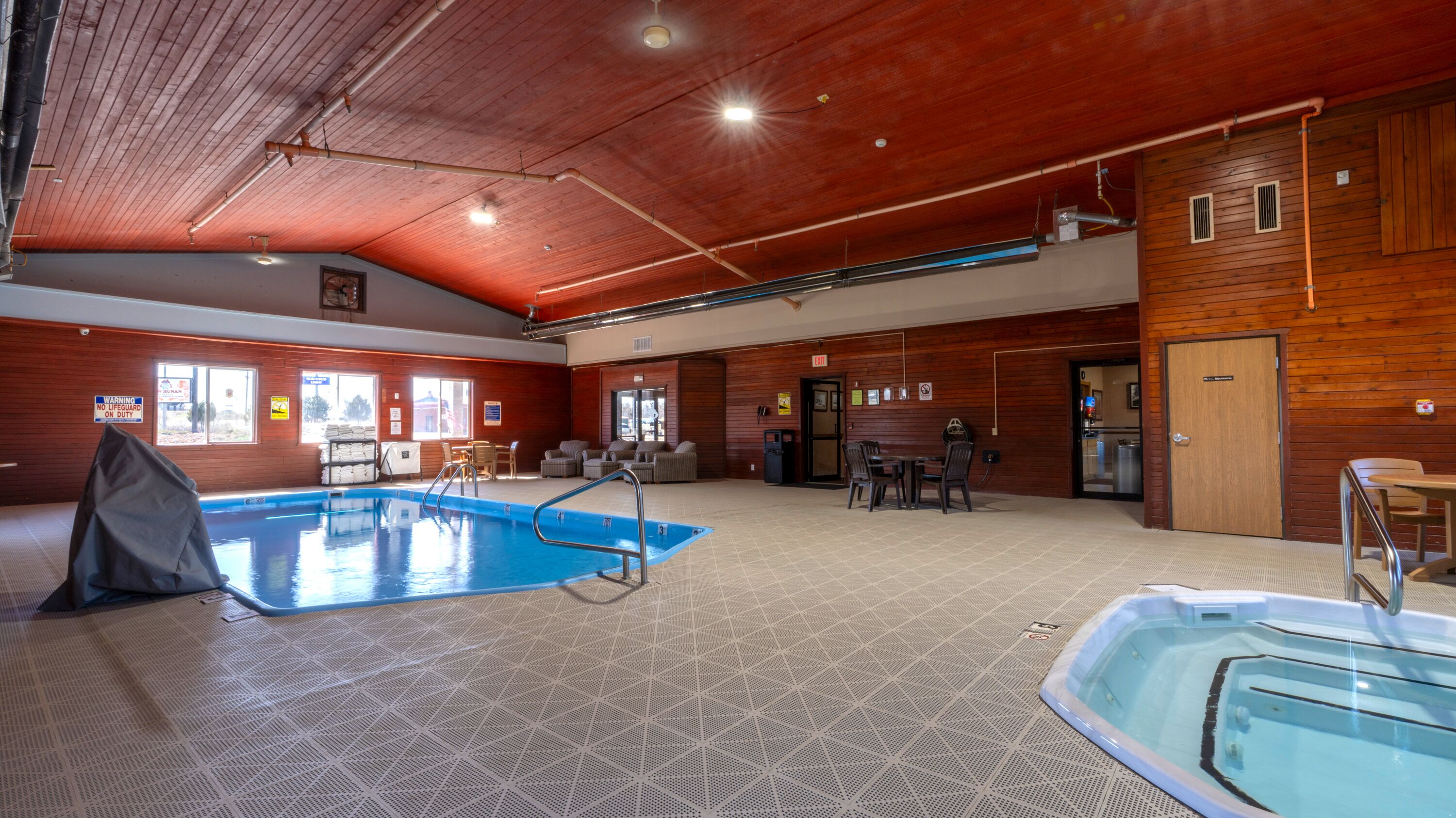 Una piscina cubierta con zona acondicionada, paredes de madera y un área de descanso con mesas y sillas.