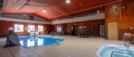 Una piscina cubierta con zona acondicionada, paredes de madera y un área de descanso con mesas y sillas.