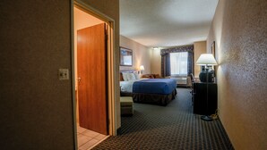 Une chambre d’hôtel avec un lit, un bureau, une chaise, une lampe et une fenêtre avec des rideaux.