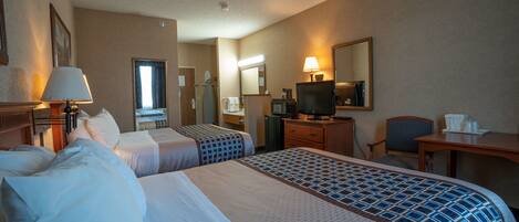 A hotel room with two beds, a desk, a television, a mirror, and a bathroom visible through a door.